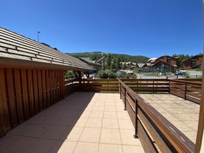A covered outdoor area with wooden railings, a tiled floor, and a view of buildings and a hill in the background.