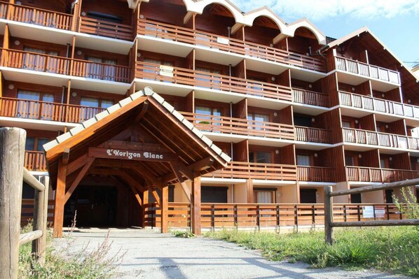 Ein mehrstöckiges Hotel mit hölzernen Balkonen und einem überdachten Eingang, auf dem "L'Horizon Blanc" steht.