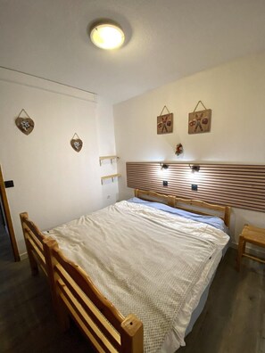 A bedroom with a wooden bed, a bedside table, a wall-mounted light, and a ceiling light. - 100m from ski lifts, Ground floor, terrace, tv, 28m², La Joue du Loup (Le Dévoluy)