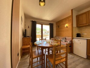 A cozy kitchen with wooden cabinets, a dining table with chairs, and a small refrigerator.