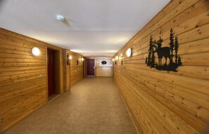 A wooden hallway with a ceiling light, a door at the end, and a wall with a silhouette of a moose and trees.