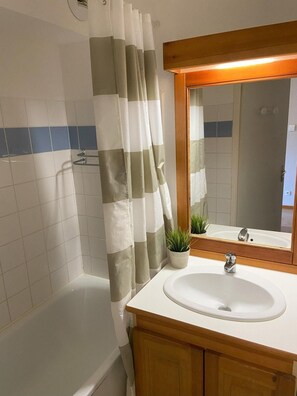 Un baño con lavamanos blanco, tocador de madera y cortina de ducha.