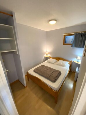 Un dormitorio pequeño y ordenado con una cama individual, mesitas de noche con lámparas, una ventana con cortinas y un armario empotrado.