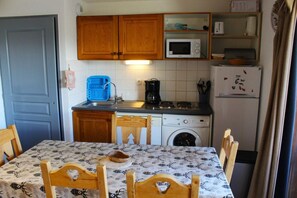 A compact kitchen with wooden cabinets, a microwave, a coffee maker, a washing machine, and a table with chairs.