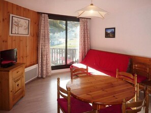 A room with a wooden dining table, chairs, a red sofa, a television on a wooden cabinet, and a large window with curtains. - Ski-in/ski-out & foot of the slopes, 2nd floor, view ski slopes, balcony, tv, 40m², Les Orres (Les Orres)