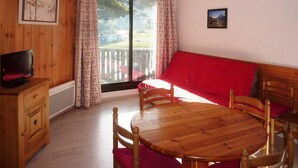 A cozy room with a wooden dining table, red sofa, and a television on a wooden cabinet.