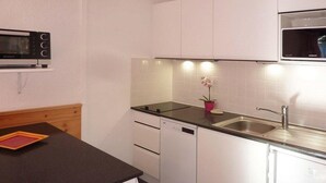 A compact kitchen with white cabinets, a black countertop, a microwave, a dishwasher, and a sink.