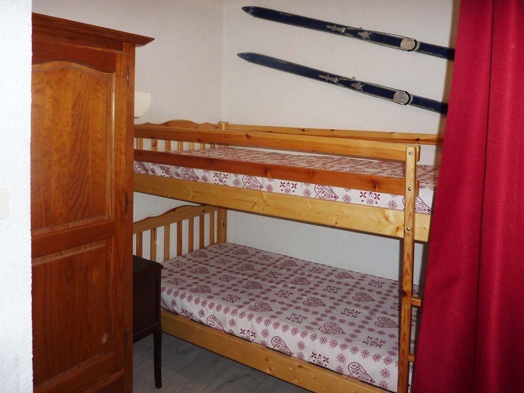 A bunk bed with a patterned mattress, a wooden wardrobe, and skis hanging on the wall.