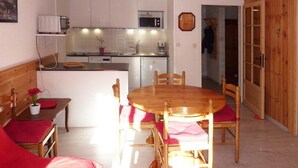 A compact kitchen with white cabinets, a microwave, and a toaster. There is a dining table with four chairs, a bench, and a wooden cabinet with glass doors.