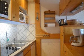 A compact kitchen with wooden cabinets, a microwave, a coffee maker, and a kettle.