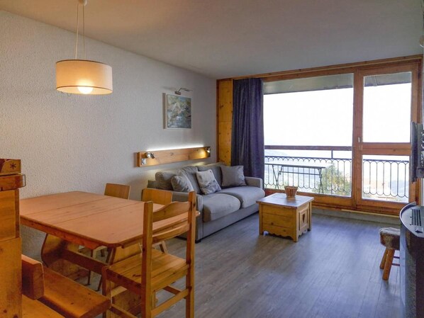 A cozy living room with a wooden dining table, sofa, and a balcony with a view.