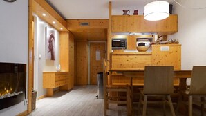 Un intérieur chaleureux en bois, avec un coin repas, une cheminée et une cuisine équipée d’appareils électroménagers modernes.