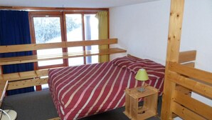A small, single-bed room with a wooden bunk bed structure, a bedside table with a lamp, and a window with curtains. - 300m from ski slopes, 5th floor, balcony, tv, 33m², Les Arcs (Les Arcs)
