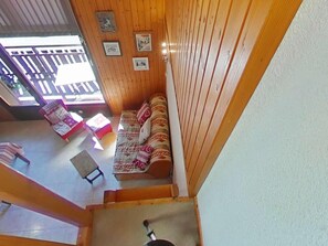 A wooden interior with a sofa and chairs, a small table, and a staircase leading to an upper level.