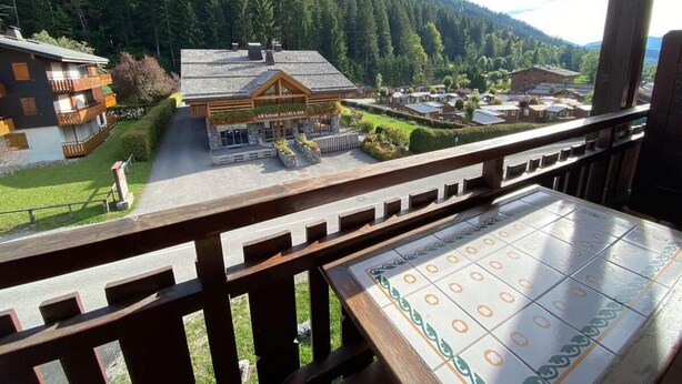 Un hotel con fachada de madera, un patio empedrado y vistas a una montaña boscosa.