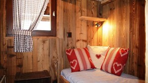 Una habitación de cabaña de madera con una cama, cortinas de cuadros y una lámpara fijada a la pared.