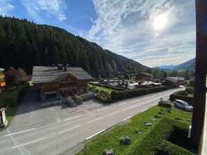 A hotel with a stone facade, a parking lot, and a road leading to a mountainous area. - 3rd floor, view mountain, balcony, tv, ski locker, 27m², Le Grand Bornand (Le Grand-Bornand)