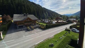 Un hotel de fachada de piedra, un estacionamiento y una carretera que conduce a una zona montañosa.