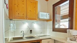 Una cocina compacta con armarios de madera, microondas, horno integrado y cafetera.