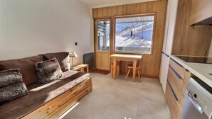 A compact room with a wooden sofa, a small table, and a view of a snowy mountain. - 10m from ski slopes, balcony, ski locker, 16m², Méribel-Mottaret (Méribel - Les Allues)