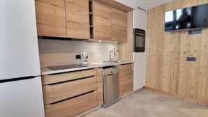 A modern kitchen with wooden cabinets, a dishwasher, a built-in oven, and a flat-screen TV mounted on the wall. - 10m from ski slopes, balcony, ski locker, 16m², Méribel-Mottaret (Méribel - Les Allues)