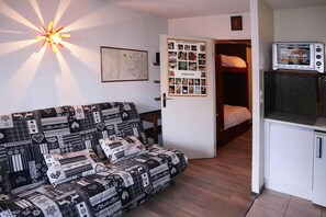 A room with a patterned sofa, a map on the wall, a door with a bulletin board, and a kitchenette with a microwave.