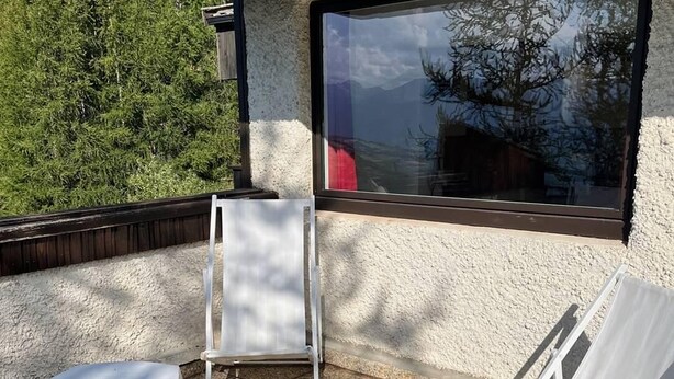 An outdoor seating area with white plastic chairs and a wooden table, a window with a view of trees, and a textured wall. - Ski-in/ski-out & foot of the slopes, 2nd floor, view ski slopes, balcony, tv, ski locker, 18m² (Les Orres)