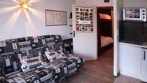 A cozy room with a patterned sofa, a map on the wall, a bulletin board with photos, and a kitchenette with a microwave. - Ski-in/ski-out & foot of the slopes, 2nd floor, view ski slopes, balcony, tv, ski locker, 18m² (Les Orres)