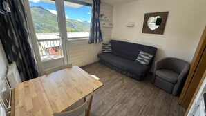Une pièce avec une table en bois, un canapé, une chaise et une vue sur les montagnes par la fenêtre.