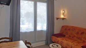 A room with a wooden dining table, two chairs, a sofa with a floral pattern, a small round side table, and a TV mounted on the wall. - Resort center, balcony, tv, 25m², Les Orres (Les Orres)