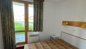 Une petite pièce avec un lit, un bureau et une fenêtre avec des rideaux.