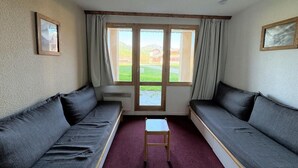 Une pièce avec deux canapés de couleur sombre, une petite table en bois et une fenêtre avec des rideaux.