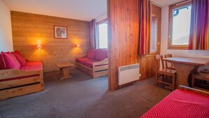 A cozy room with wooden walls, a red sofa, a small table, a chair, and a wooden desk with chairs. - 200m from ski slopes, 1st floor, balcony, ski locker, 31m², Valmorel (Valmorel)