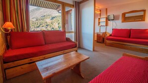 A cozy room with a wooden sofa, a small table, and a view of a mountainous landscape through a window. - 200m from ski slopes, 1st floor, balcony, ski locker, 31m², Valmorel (Valmorel)