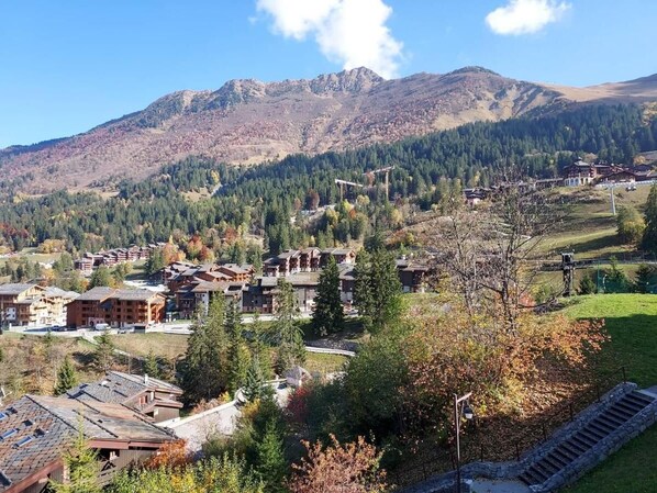 Un complejo turístico de montaña con varias edificaciones de estilo chalet, un telesilla y vistas a las montañas boscosas circundantes.