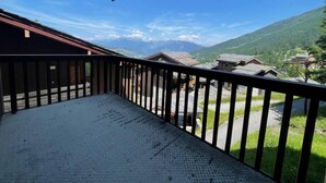 Ein Balkon mit Metallgeländer, der auf eine gebirgige Landschaft und ein Dorf darunter blickt.