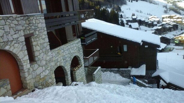 Ein mit Schnee bedecktes Berghotel mit Steinarchitektur, einem Balkon und Blick auf ein verschneites Dorf.