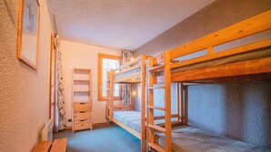 Ein Schlafraum mit Etagenbetten, einem Holztisch, einem Stuhl und einem Fenster mit Vorhängen.