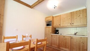A compact kitchen with wooden cabinets, a dining table with chairs, and a microwave. - 150m from ski slopes, 2nd floor, fitness, swimming pool, balcony, tv, ski locker, 32m², Val Cenis (Lanslebourg-Mont-Cenis)
