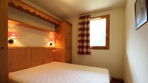 A bedroom with a wooden headboard, a bed with a quilt, two wall-mounted lamps, a window with a plaid curtain, and a framed picture on the wall. - 150m from ski slopes, 2nd floor, fitness, swimming pool, balcony, tv, ski locker, 32m², Val Cenis (Lanslebourg-Mont-Cenis)