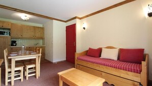 A compact living space with a wooden dining table, a sofa with red cushions, and a kitchenette in the background. - 150m from ski slopes, 2nd floor, fitness, swimming pool, balcony, tv, ski locker, 32m², Val Cenis (Lanslebourg-Mont-Cenis)