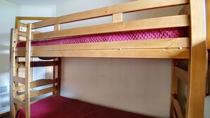 Un lit superposé avec une structure en bois et un matelas rouge.
