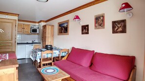 Une cuisine de taille réduite avec des meubles en bois, une table à manger avec des chaises et un canapé rouge.