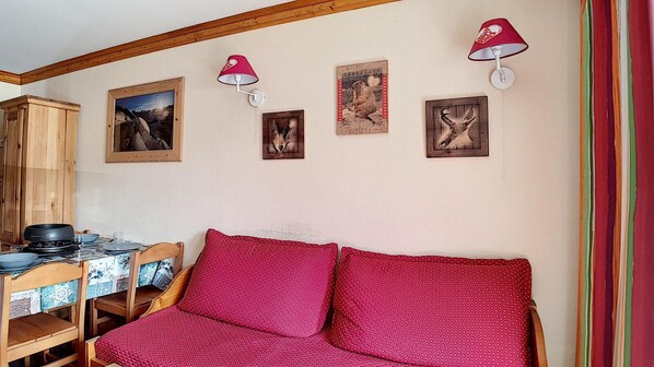 Une pièce chaleureuse avec un meuble en bois, une table à manger avec des chaises, un canapé rouge et des lampes fixées au mur.
