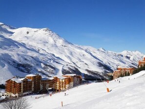 Une montagne enneigée abritant une station de ski, avec des bâtiments à plusieurs étages dotés de balcons, qui proposent probablement des hébergements et des installations pour les sports d’hiver.