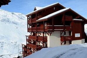 Un chalet en bois doté de plusieurs balcons, situé au pied d’une montagne enneigée.