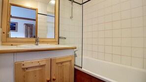 Une salle de bain avec un meuble-lavabo en bois, un miroir, un lavabo et un espace douche.