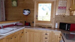 A wooden kitchen with a large window, wooden cabinets, a sink, and a microwave.