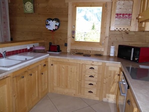 A wooden kitchen with a large window, wooden cabinets, a sink, and a microwave. - 1st floor, terrace, balcony, fireplace or stove, parking, tv, 158m², Pralognan-la-Vanoise (Pralognan-la-Vanoise)