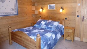 A wooden room with a bed, two wall-mounted lamps, and a framed picture.